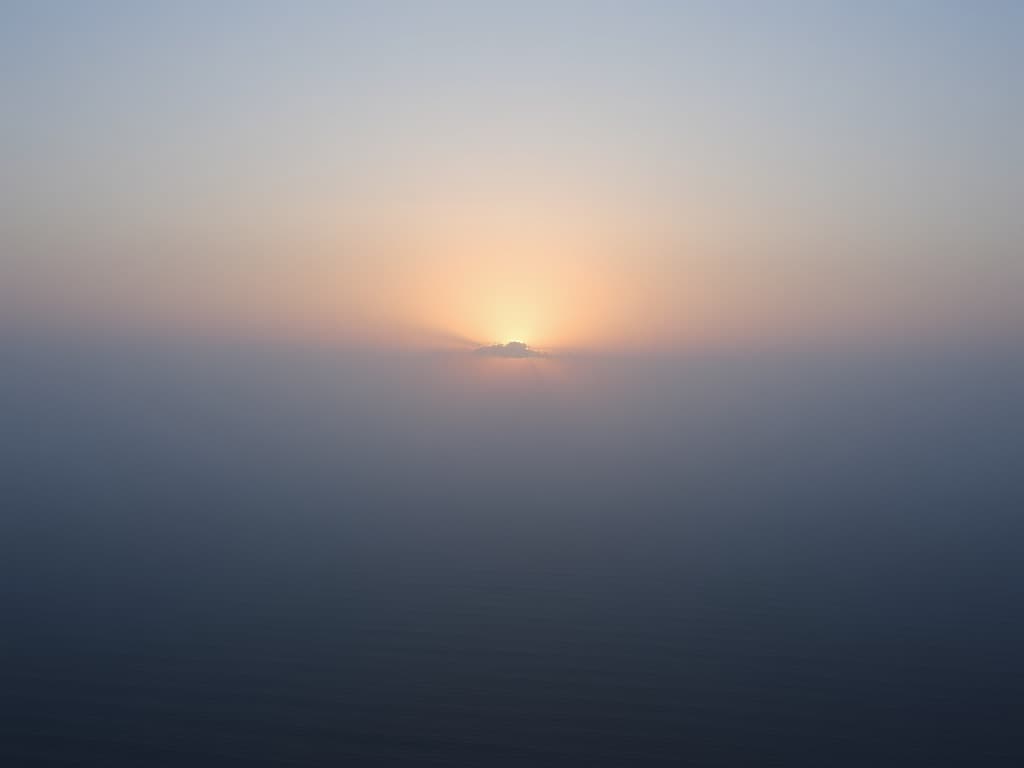 Coastal horizon at dawn, low sun cutting through thin sea haze